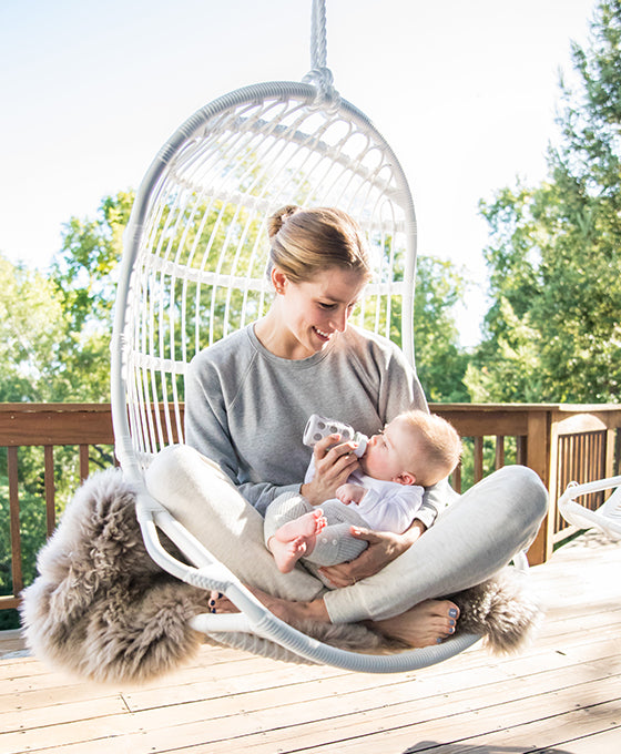 Woman sitting outside in chair while using a Lifefactory baby bottle to feed a baby.