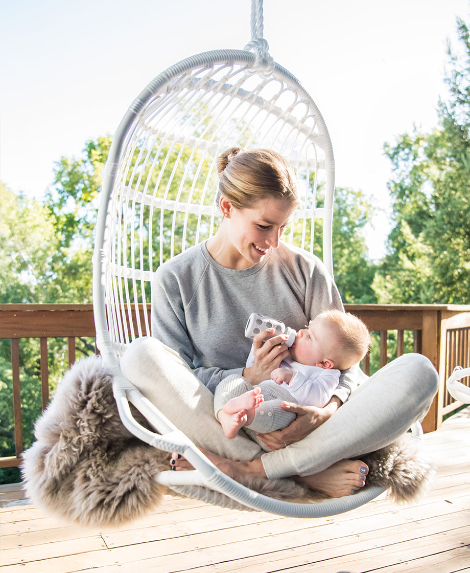 Woman sitting outside in chair while using a Lifefactory baby bottle to feed a baby.