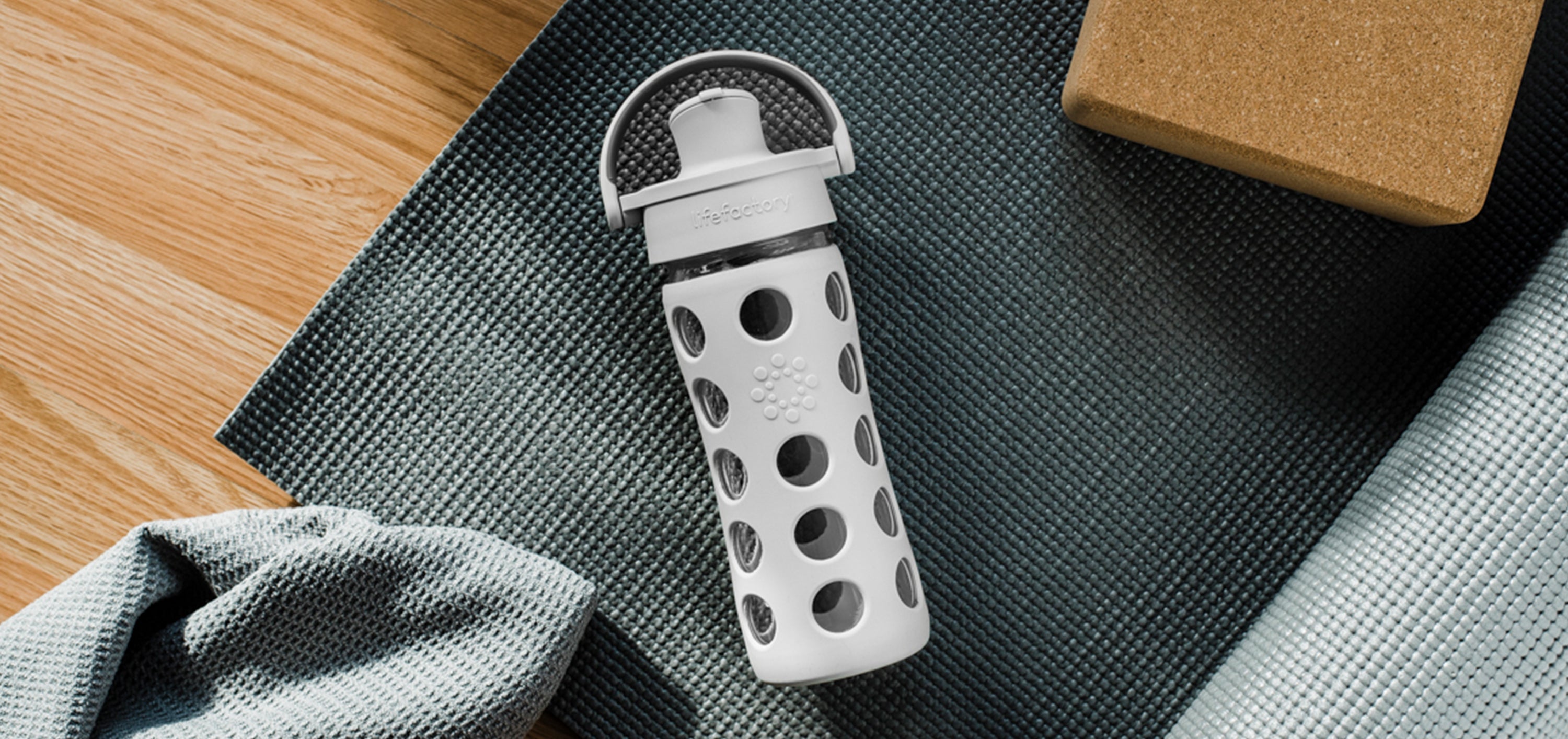 Lifefactory glass water bottle laying on a yoga mat.
