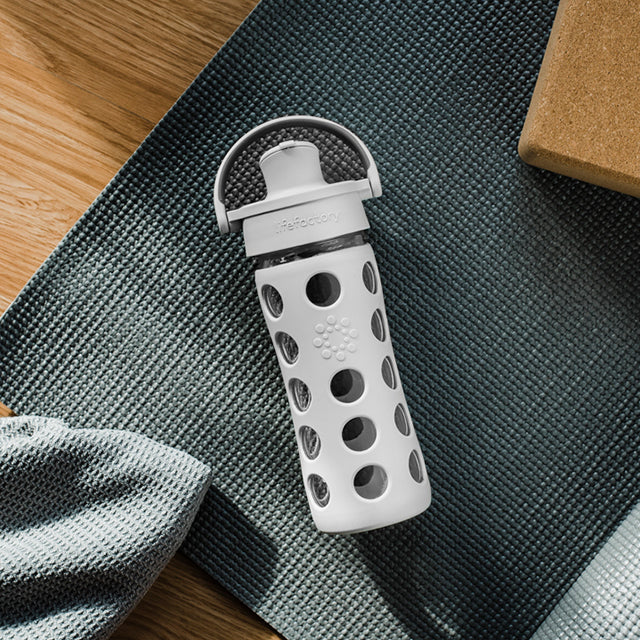 Lifefactory glass water bottle laying on a yoga mat.