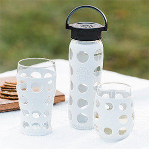 Lifefactory beer glass, 22 ounce glass water bottle with flat lid, and stemless wine glass on an outdoor table.