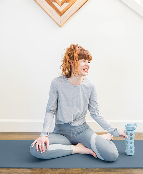 Woman sitting on yoga mat with a Lifefactory glass water bottle.