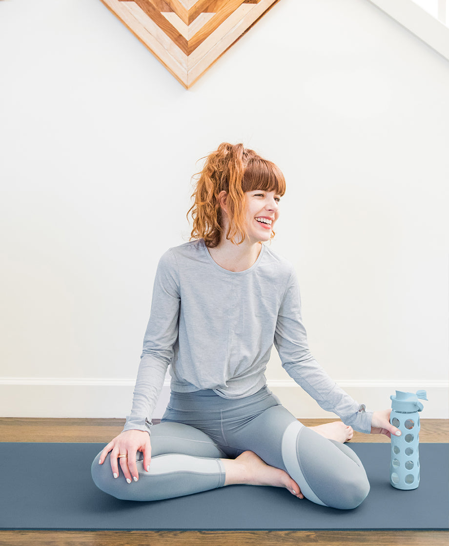 Woman sitting on yoga mat with a Lifefactory glass water bottle.