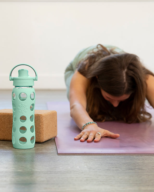 Woman doing yoga with a Lifefactory glass water bottle next to her.