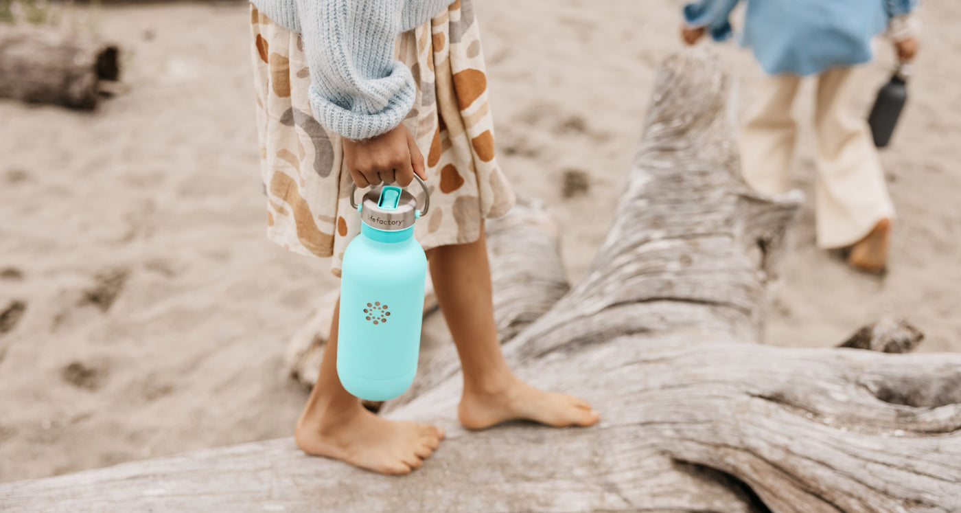 A girl walking on a beach holding a Lifefactory water bottle