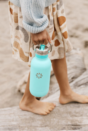 A girl walking on a beach holding a Lifefactory water bottle