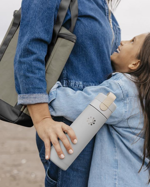 Two children on a beach with one holding a water bottle