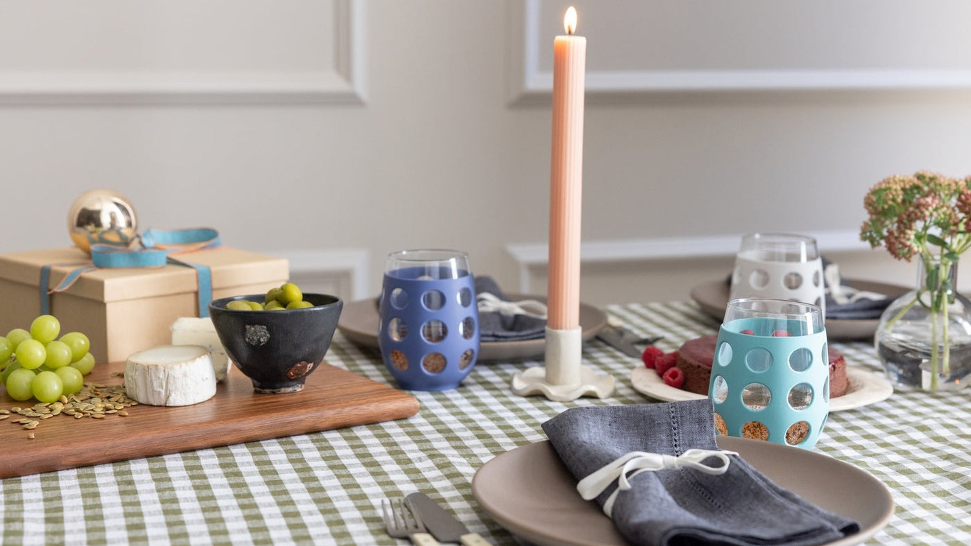 Dining table setting with checkered tablecloth, plates, Lifefactory wine glasses, and candles.