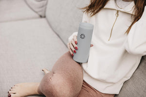 Person holding a Life factory gray tumbler with a logo on a beige couch